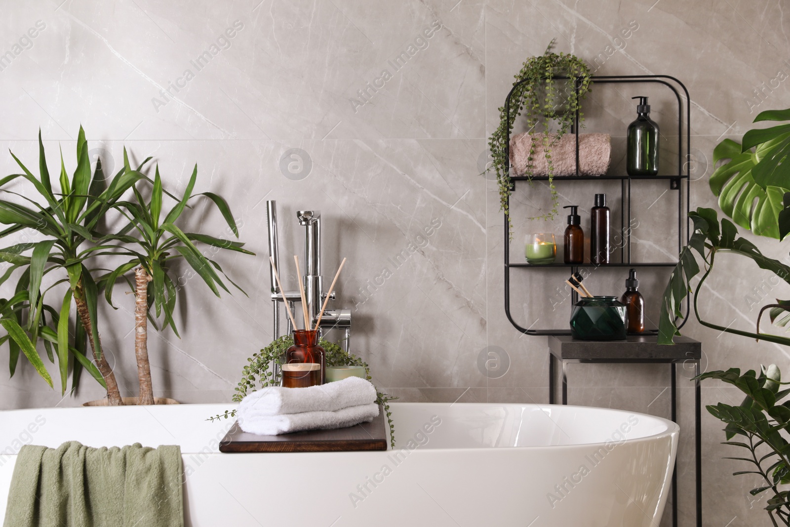 Photo of Modern white tub and beautiful green houseplants in bathroom. Interior design