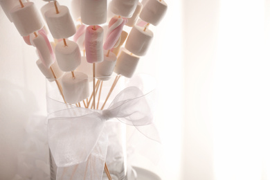 Photo of Tasty marshmallow on wooden sticks with bow for birthday party on blurred background, closeup