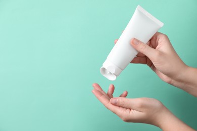 Photo of Woman applying cosmetic cream from tube onto her hand on turquoise background, closeup. Space for text