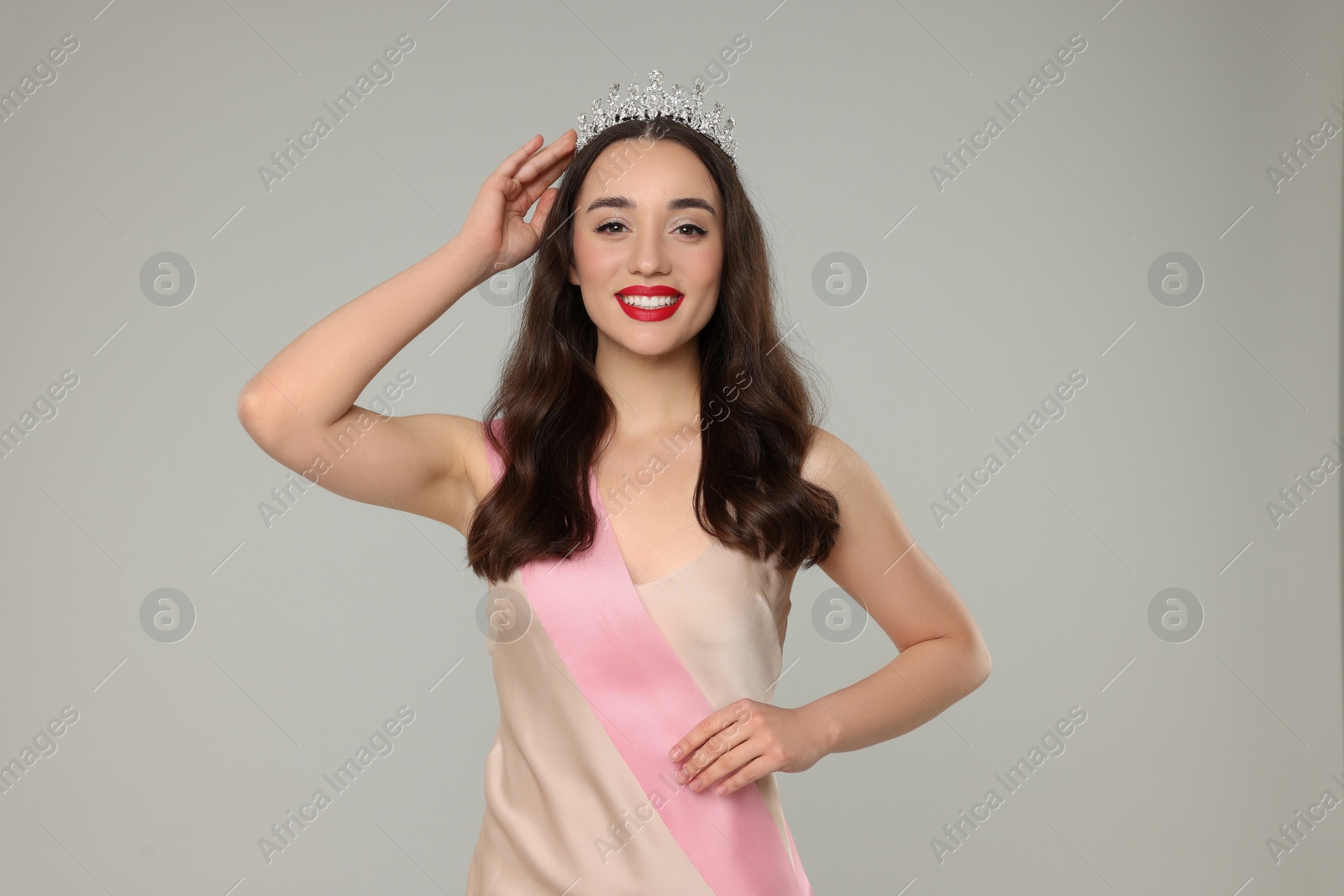 Photo of Beautiful young woman with tiara and ribbon in dress on grey background. Beauty contest