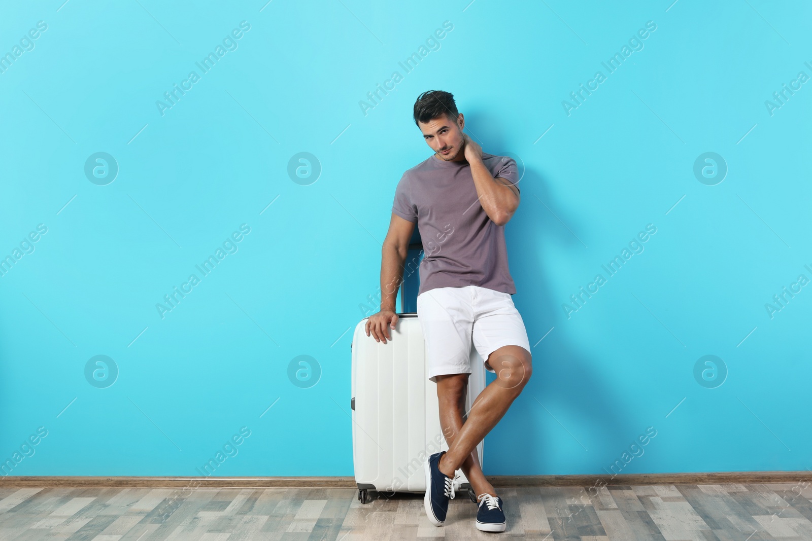 Photo of Young man with suitcase on color wall background