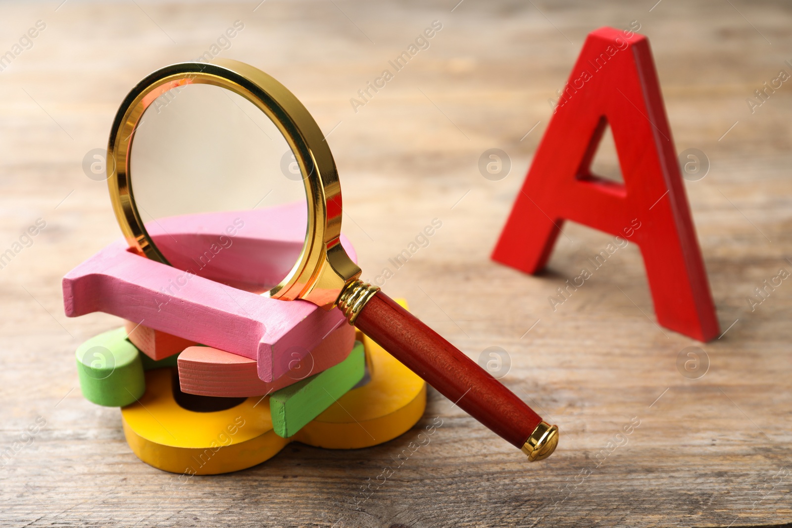 Photo of Different color letters and magnifier glass on wooden background, closeup. Find keywords concept