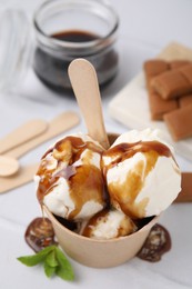 Scoops of ice cream with caramel sauce in paper cup on white table