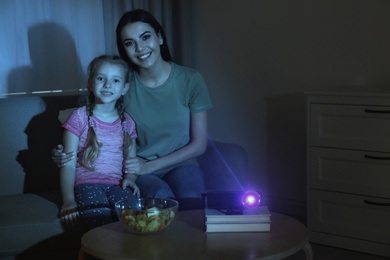 Photo of Young woman and her daughter watching movie using video projector at home