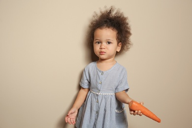 Photo of Cute African-American girl with carrot on color background