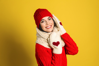 Photo of Young woman wearing warm sweater, scarf, mittens and hat on yellow background. Winter season
