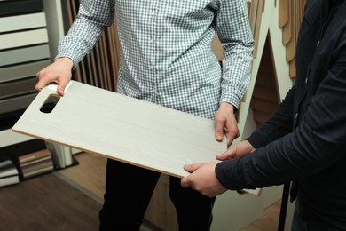 Men holding sample of wooden flooring in shop, closeup