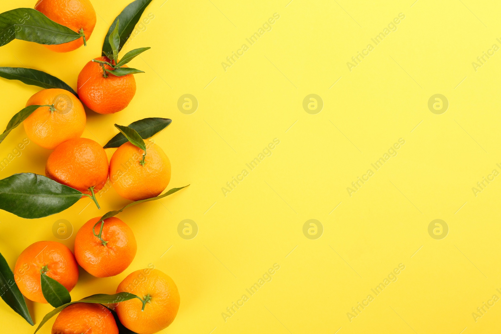 Photo of Fresh tangerines with green leaves on yellow background, flat lay. Space for text