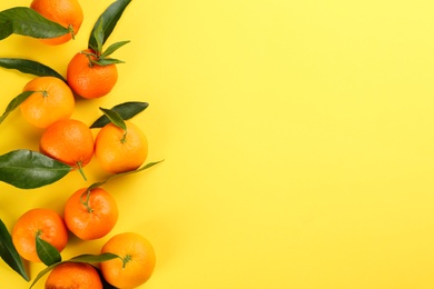 Fresh tangerines with green leaves on yellow background, flat lay. Space for text