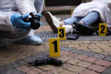 Photo of Criminologist taking photo of evidence at crime scene with dead body outdoors, closeup. Space for text