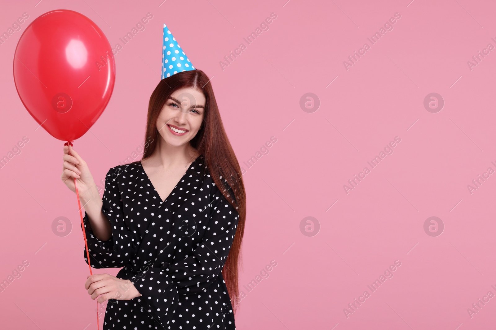 Photo of Happy woman in party hat with balloon on pink background, space for text