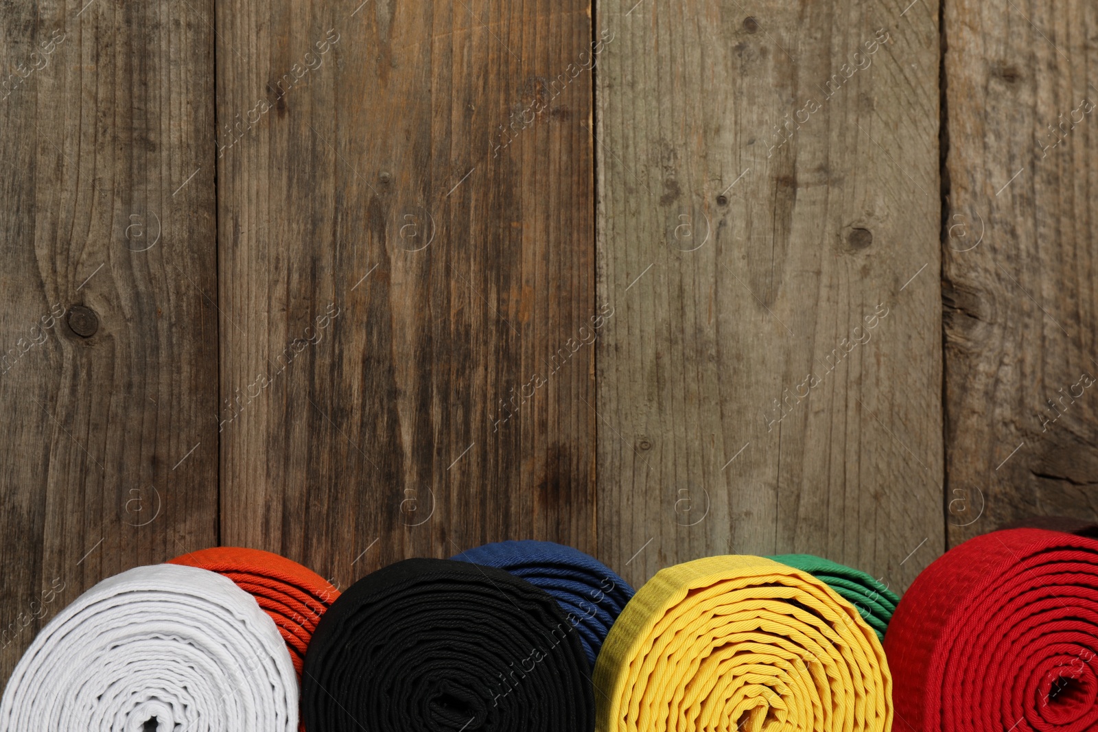 Photo of Colorful karate belts on wooden background, top view. Space for text