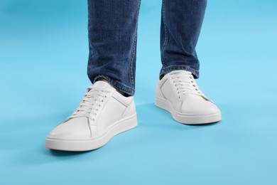 Man wearing stylish white sneakers on light blue background, closeup