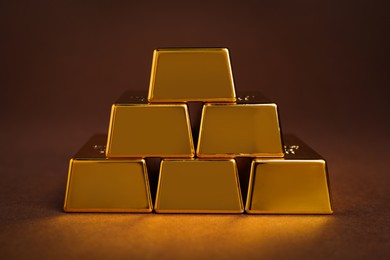 Stack of shiny gold bars on brown background