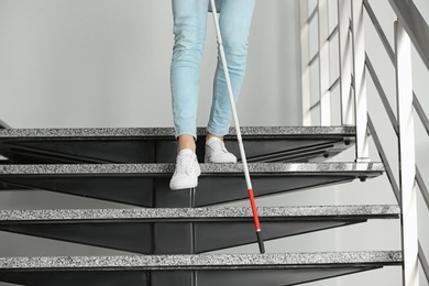 Photo of Blind person with long cane going down stairs indoors, closeup
