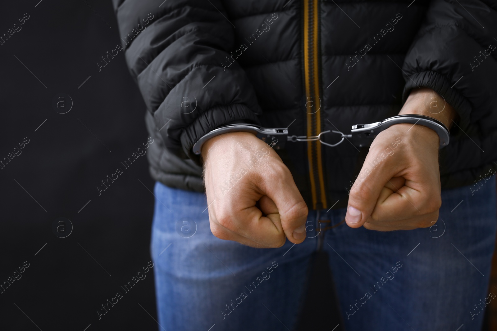 Photo of Man detained in handcuffs against dark background, closeup. Criminal law