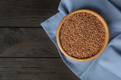 Photo of Uncooked buckwheat in bowl on wooden table, flat lay. Space for text