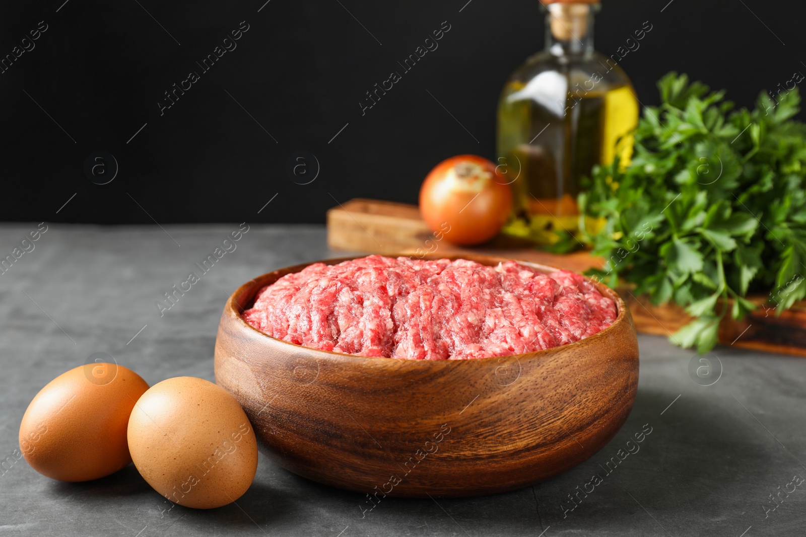 Photo of Raw ground meat in bowl and different products on grey table