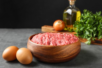 Raw ground meat in bowl and different products on grey table