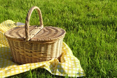 Photo of Picnic basket with checkered tablecloth on green grass outdoors, space for text