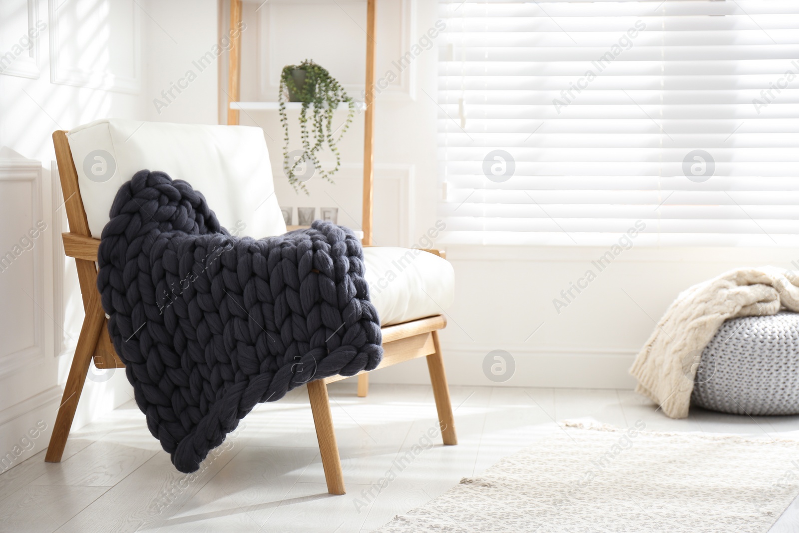 Photo of Knitted merino wool plaid on armchair in room. Space for text