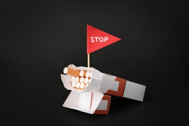 Cigarettes in pack and red flag with word Stop on black background. Quitting smoking concept