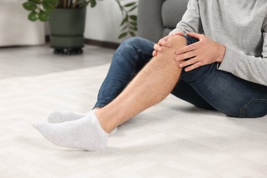 Photo of Man suffering from leg pain on white carpet at home, closeup