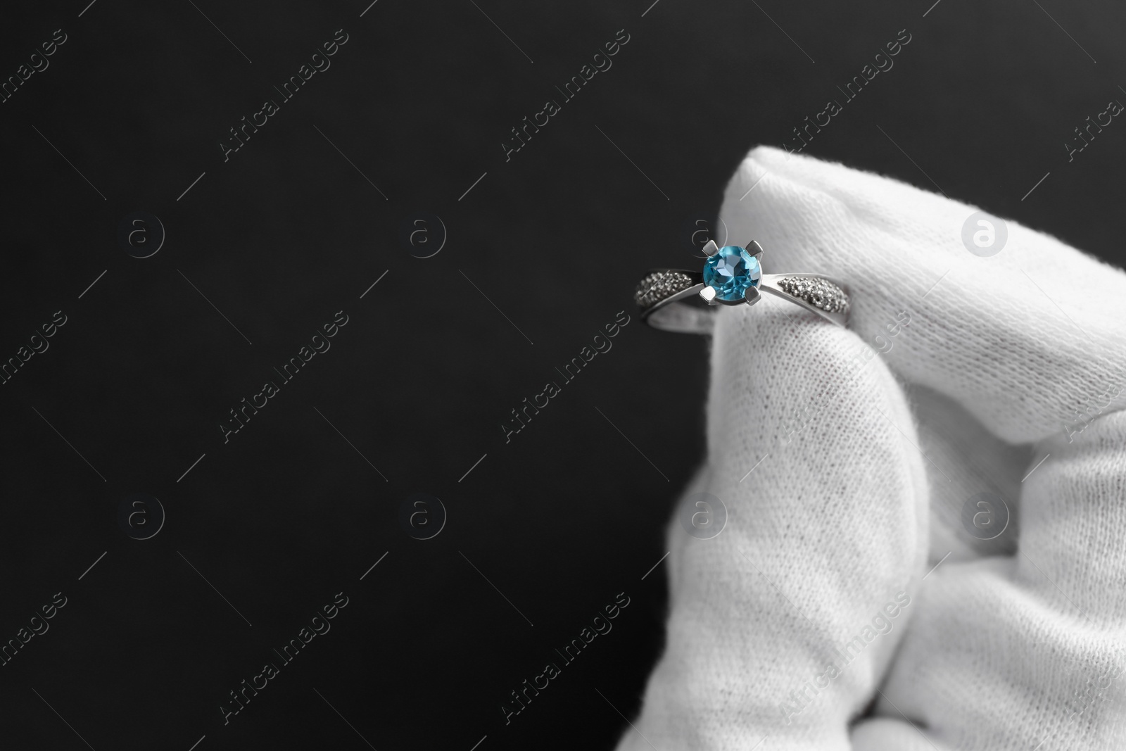 Photo of Jeweler holding topaz ring on dark grey background, closeup. Space for text