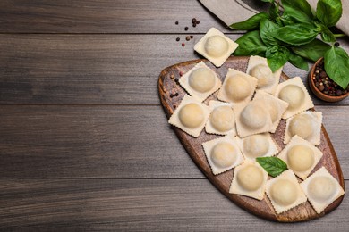 Photo of Uncooked ravioli, basil and peppercorns on wooden table, flat lay. Space for text