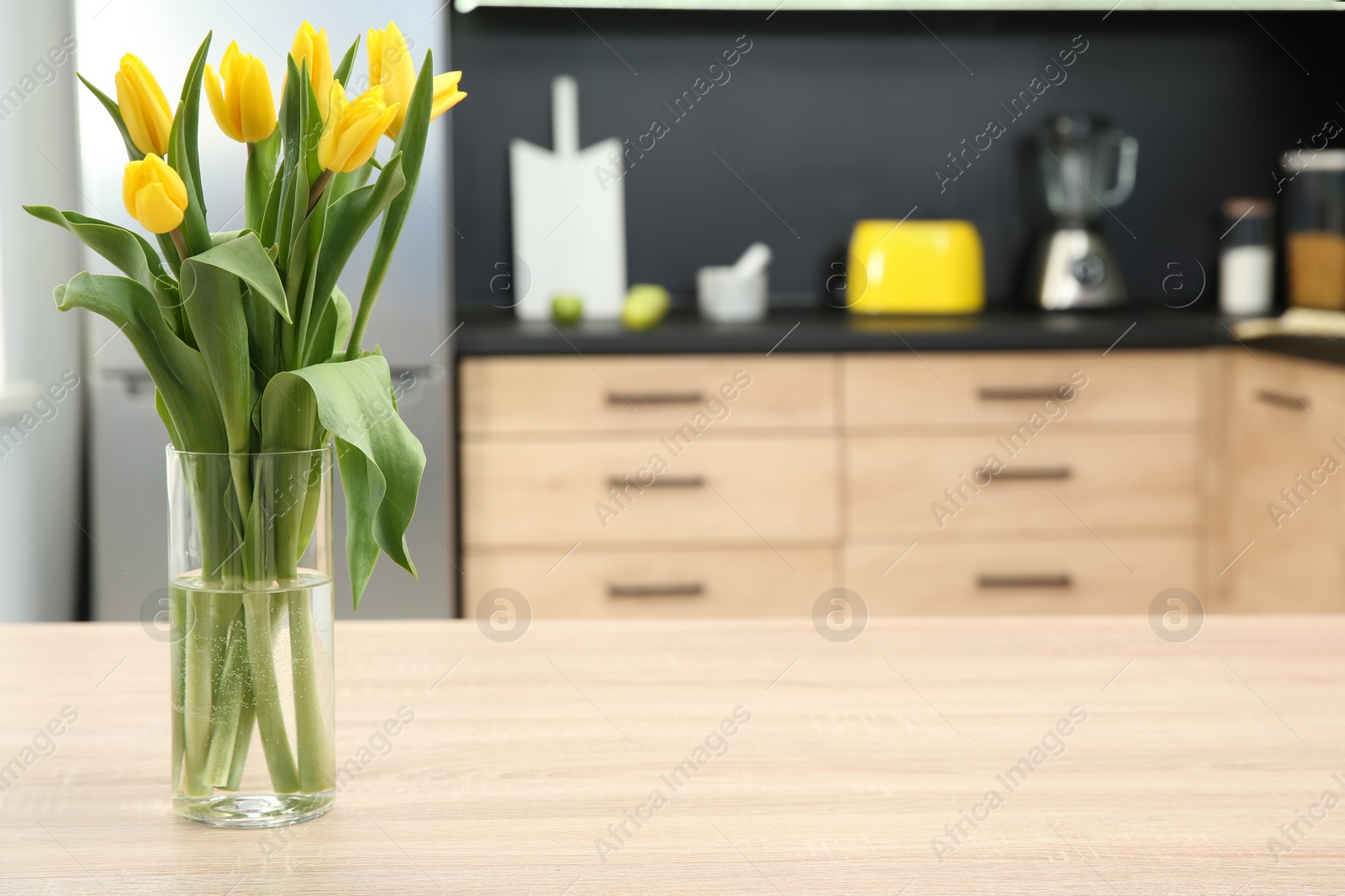 Photo of Glass vase with tulips on table in kitchen