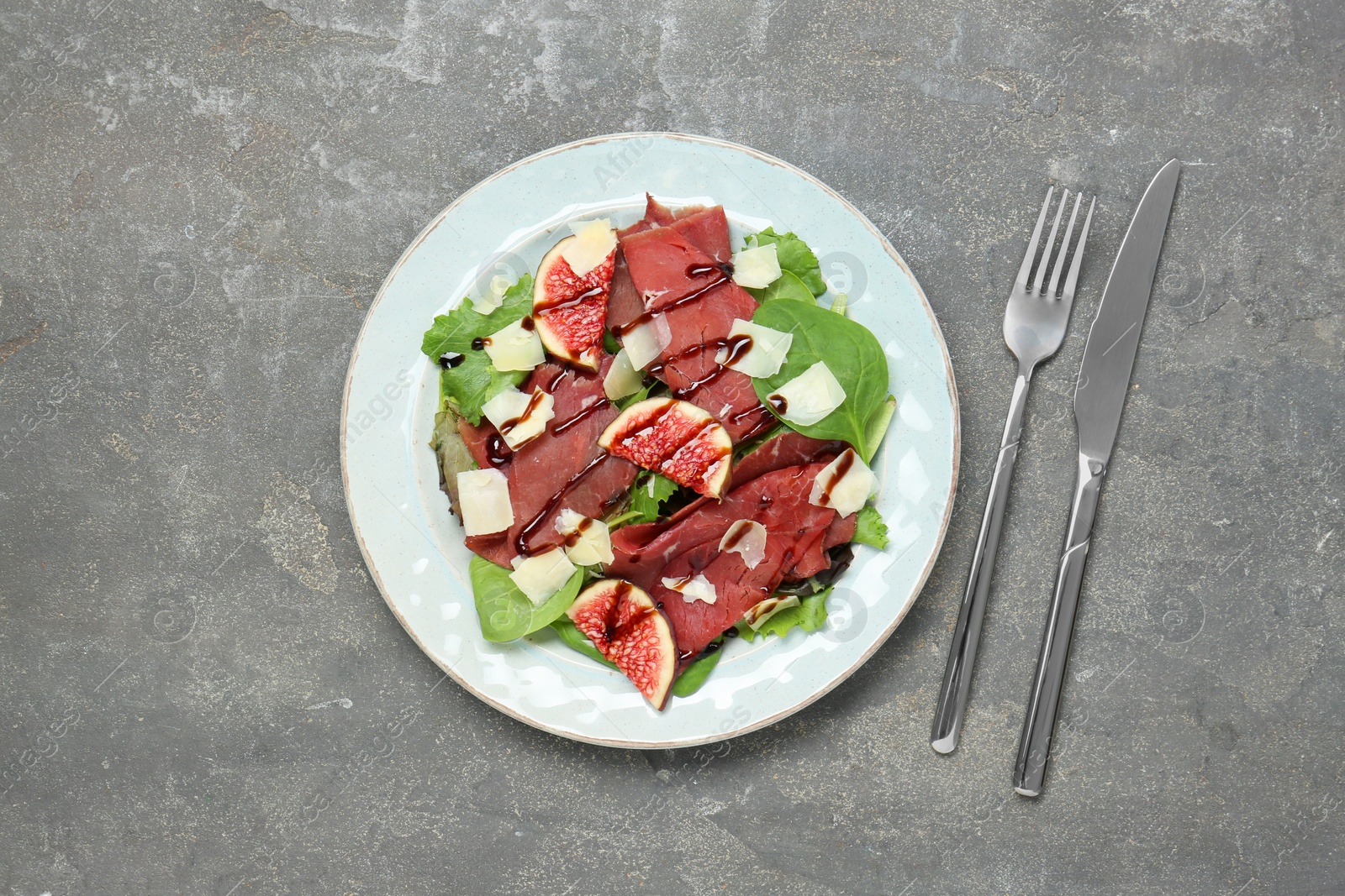 Photo of Plate with delicious bresaola salad served on grey textured table, flat lay