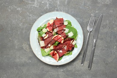 Photo of Plate with delicious bresaola salad served on grey textured table, flat lay