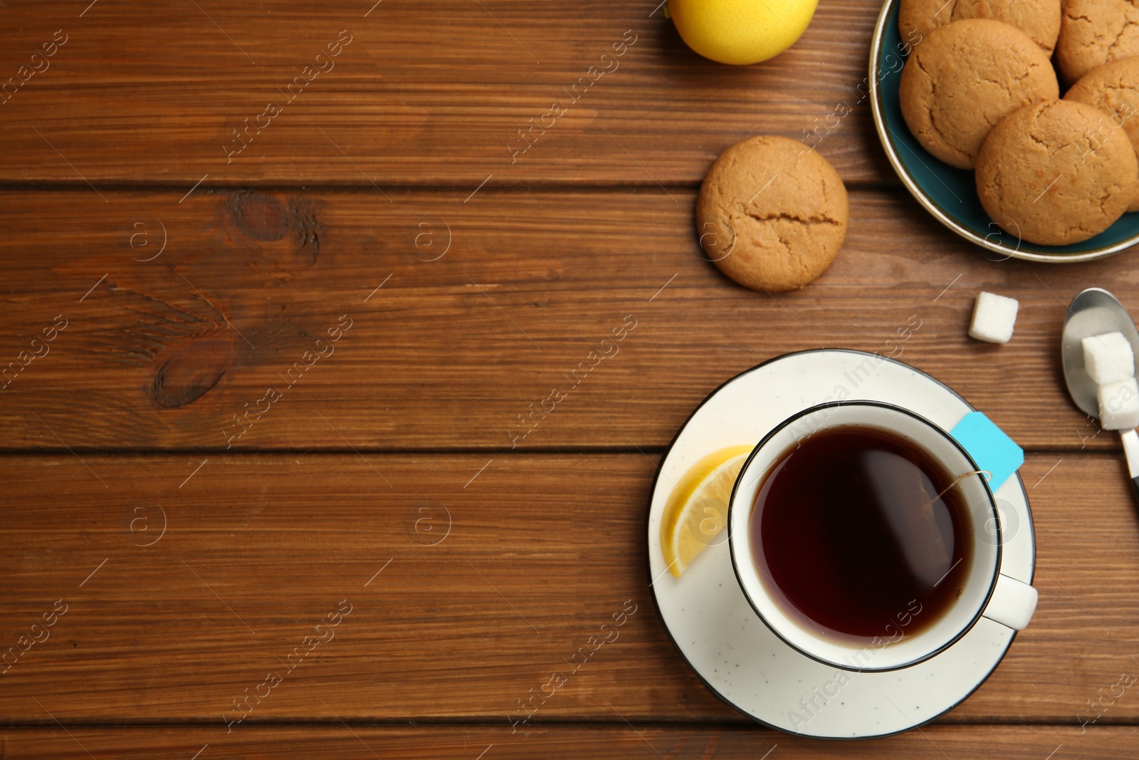 Photo of Flat lay composition with tea bag in ceramic cup of hot water, cookies and lemon on wooden table. Space for text