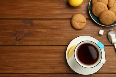 Photo of Flat lay composition with tea bag in ceramic cup of hot water, cookies and lemon on wooden table. Space for text