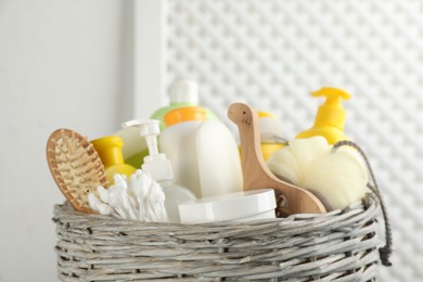 Photo of Wicker basket full of different baby cosmetic products, accessories and toy on blurred background, closeup