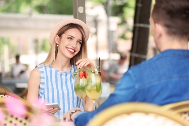 Young couple with glasses of tasty lemonade in open-air cafe