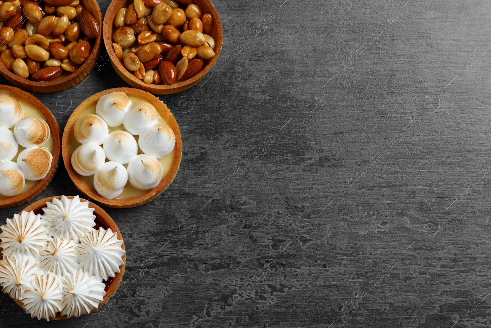 Photo of Many different tartlets on dark grey table, flat lay with space for text. Tasty dessert