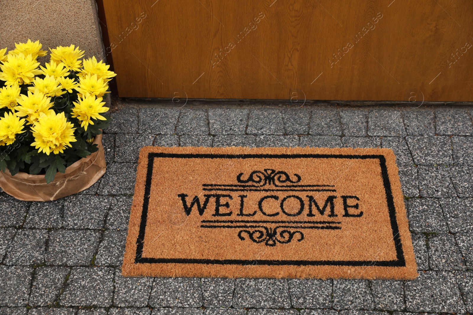 Photo of Doormat with word Welcome and beautiful flowers on floor near entrance