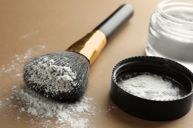 Photo of Makeup brush and lid with rice loose face powder on brown background, closeup