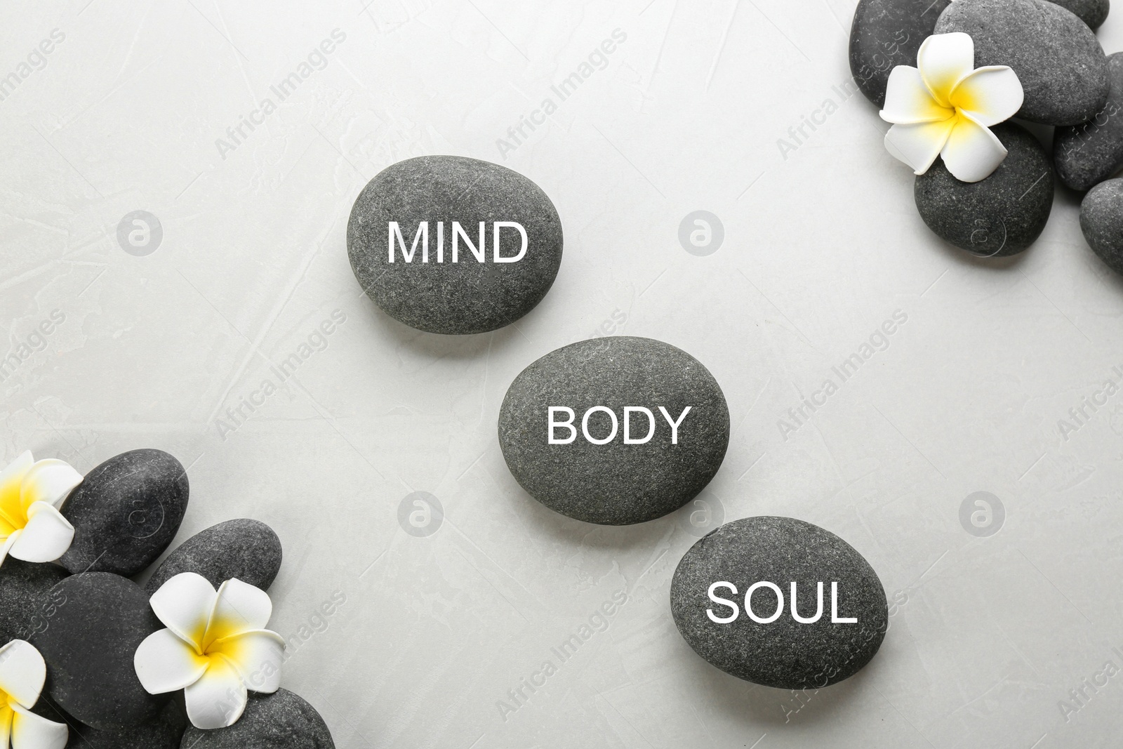 Photo of Stones with words MIND, BODY, SOUL and flowers on light background, flat lay. Zen lifestyle