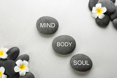 Stones with words MIND, BODY, SOUL and flowers on light background, flat lay. Zen lifestyle