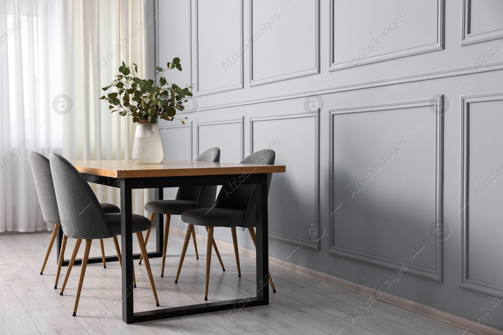 Photo of Soft chairs, table and vase with eucalyptus branches in stylish dining room. Space for text