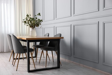 Soft chairs, table and vase with eucalyptus branches in stylish dining room. Space for text