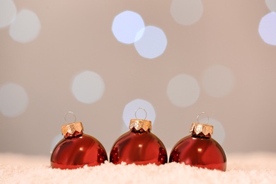 Photo of Beautiful red Christmas balls on snow against blurred festive lights. Space for text