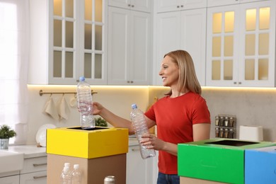 Garbage sorting. Smiling woman throwing plastic bottle into cardboard box in kitchen