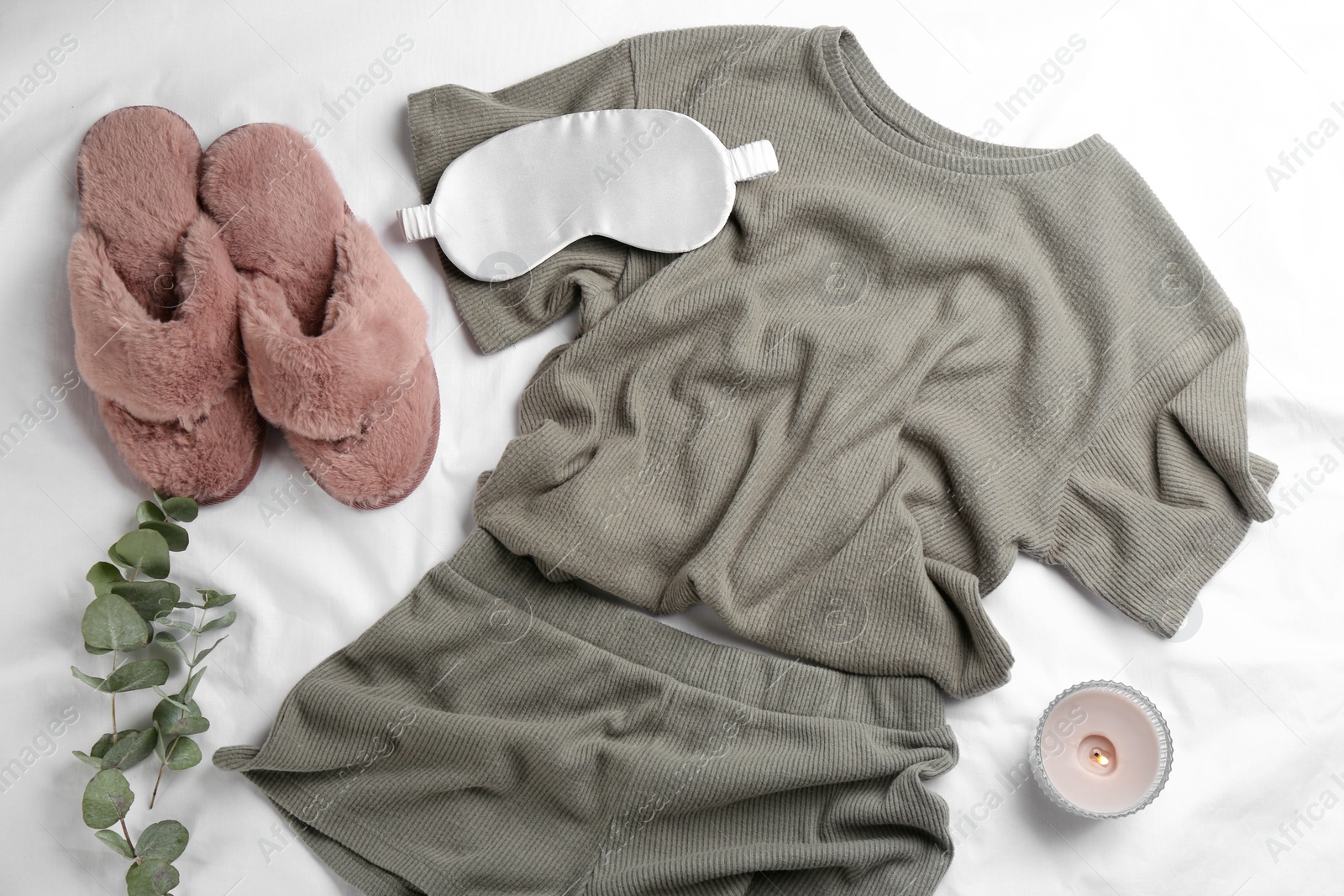 Photo of Flat lay composition with fluffy slippers and pajamas on white bedsheet. Comfortable home outfit