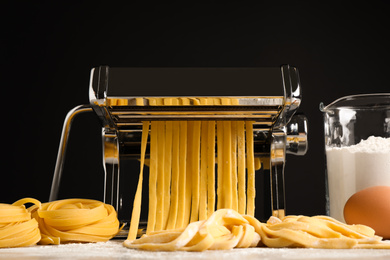 Pasta maker machine with dough and products on grey table against black background