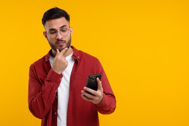 Handsome young man using smartphone on yellow background, space for text