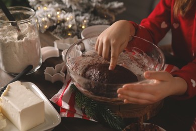 Photo of Little child making Christmas cookies at wooden table, closeup