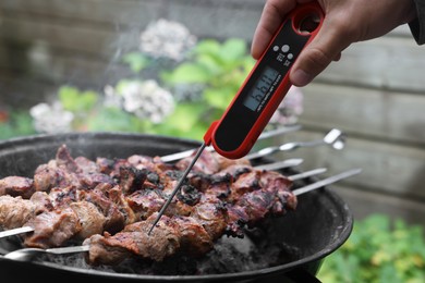 Photo of Man measuring temperature of delicious kebab on metal brazier outdoors, closeup